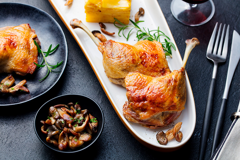 Duck legs confit with potato gratin and mushroom on a plate. Close up.